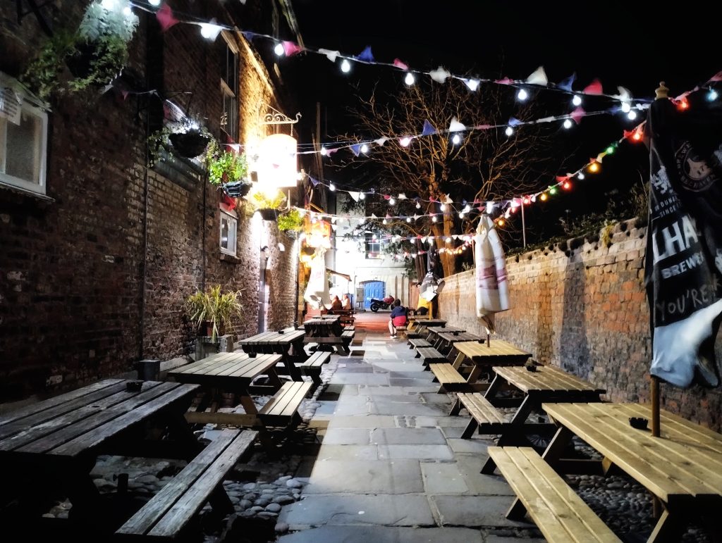 Photo of an alleyway with pub tables, and bunting and string lights above.