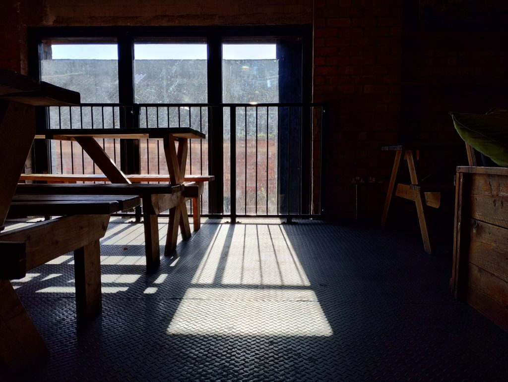 Photo: sunlight shining through a window onto the floor, between picnic-style tables and benches.