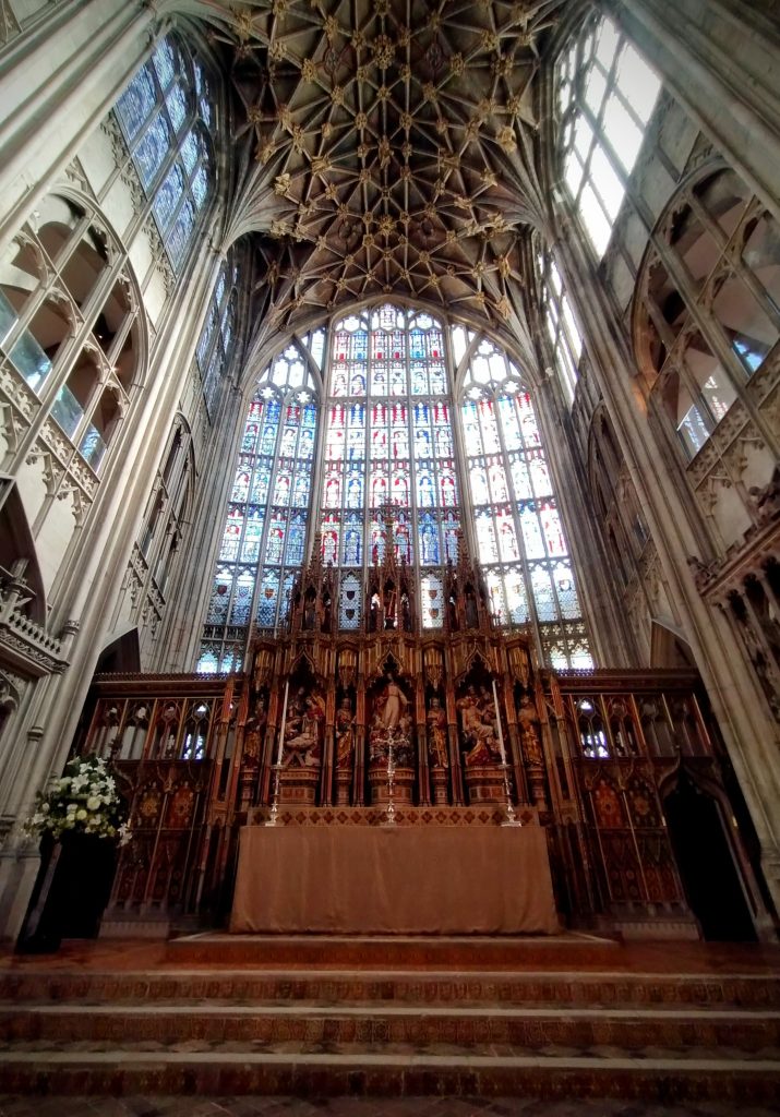 Photo: cathedral interior with vast stained glass window, altar, and ornate ceiling above.