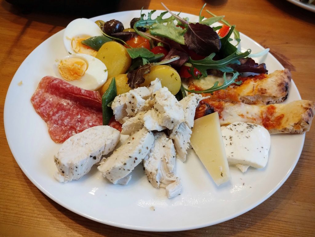 Photo: a plate of food including herbed sliced chicken, salami, potato and green bean salad, pizza, mozzarella, boiled egg, olives.