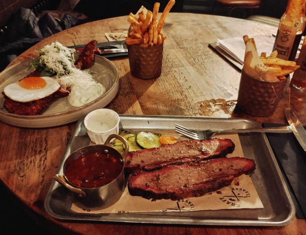 Photot: a metal platter of food - beef brisket slices plus pot of pit beans, blue cheese sauce, pickles. Fries on the side.