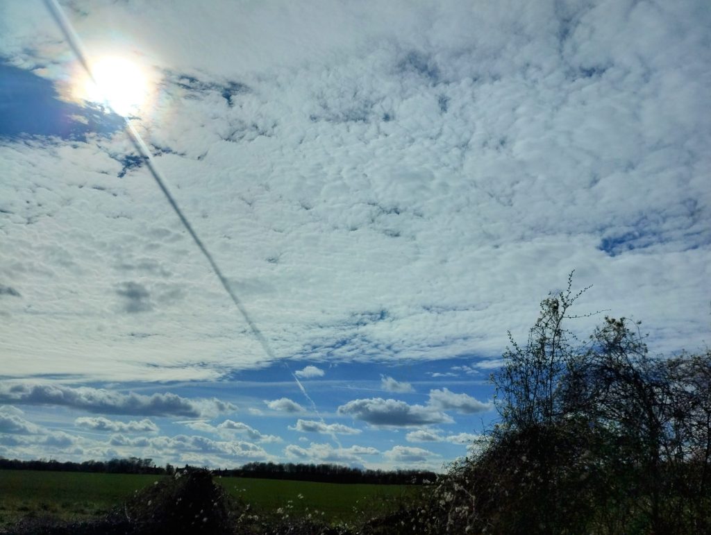 Little Joys: photo of white sheet clouds in a blue sky with the sun glowing through, and a dark shadowy line across the whole cloud.
